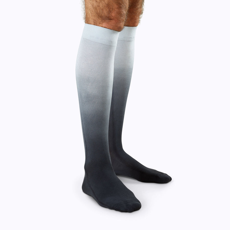 Side view of a pair of legs wearing knee-high compression socks in black ombre