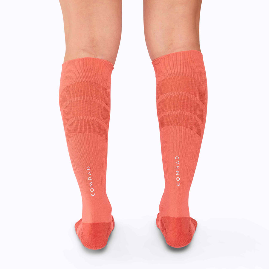 Back view of  feet wearing an athletic knee high performance blend socks coral solid