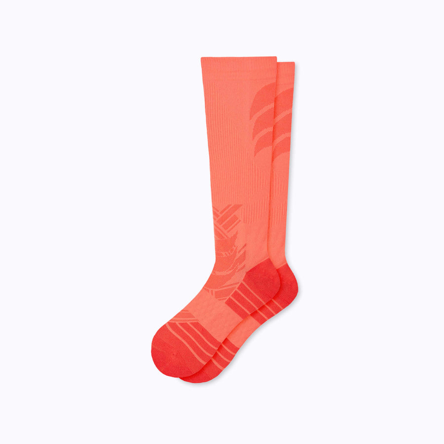 A pair of  feet wearing an athletic knee high performance blend socks coral solid