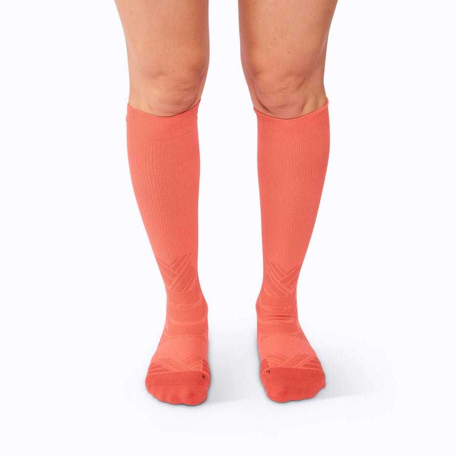 Front view of  feet wearing an athletic knee high performance blend socks coral solid