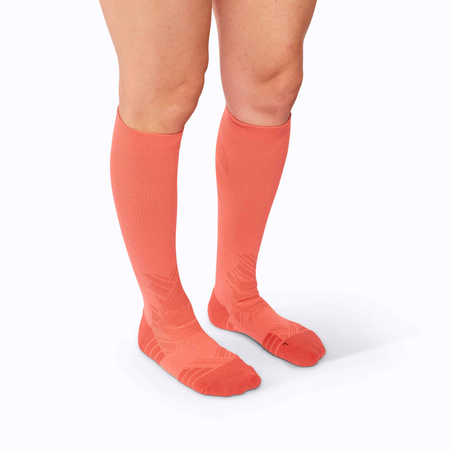 Side view of  feet wearing an athletic knee high performance blend socks coral solid