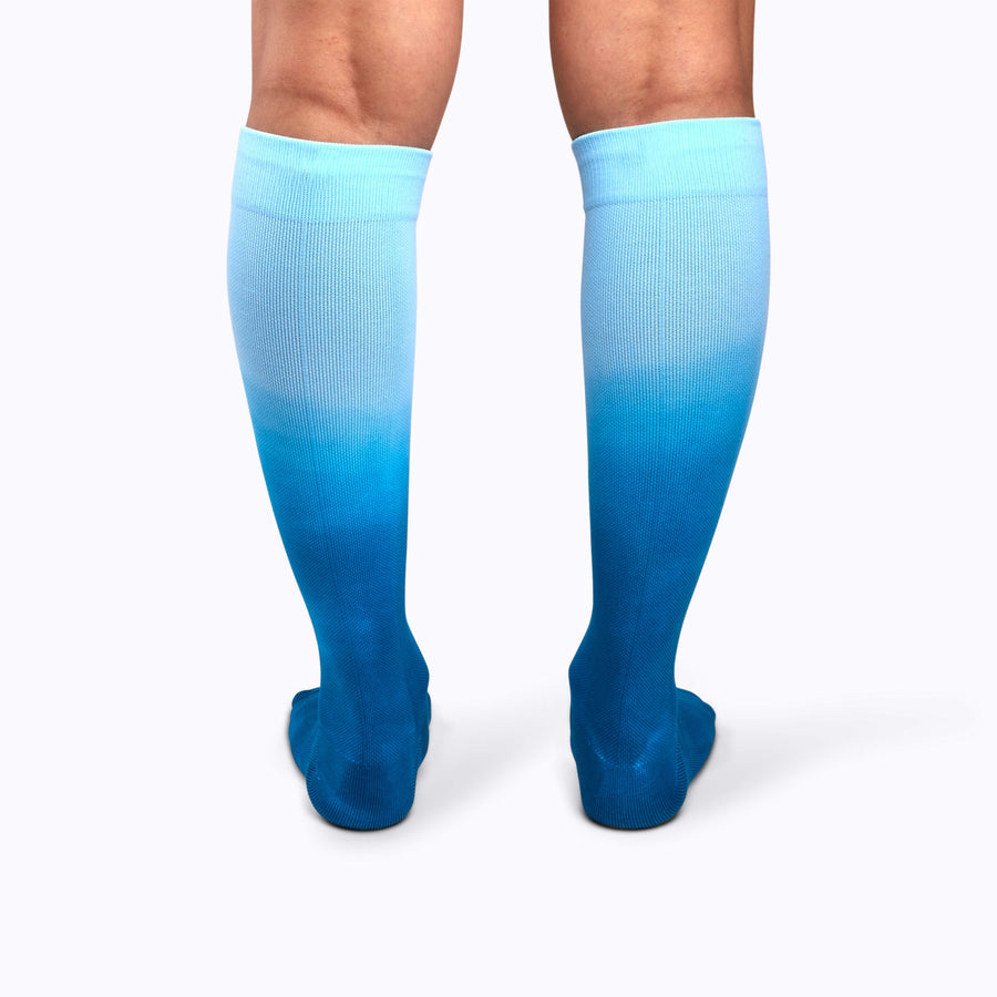 Back view of a pair of legs wearing knee-high compression socks in teal ombre