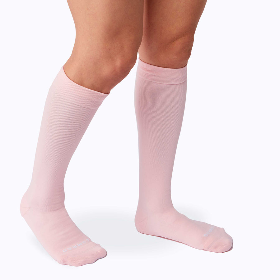 Side view of legs wearing a pair of nylon knee high compression socks in rose solid