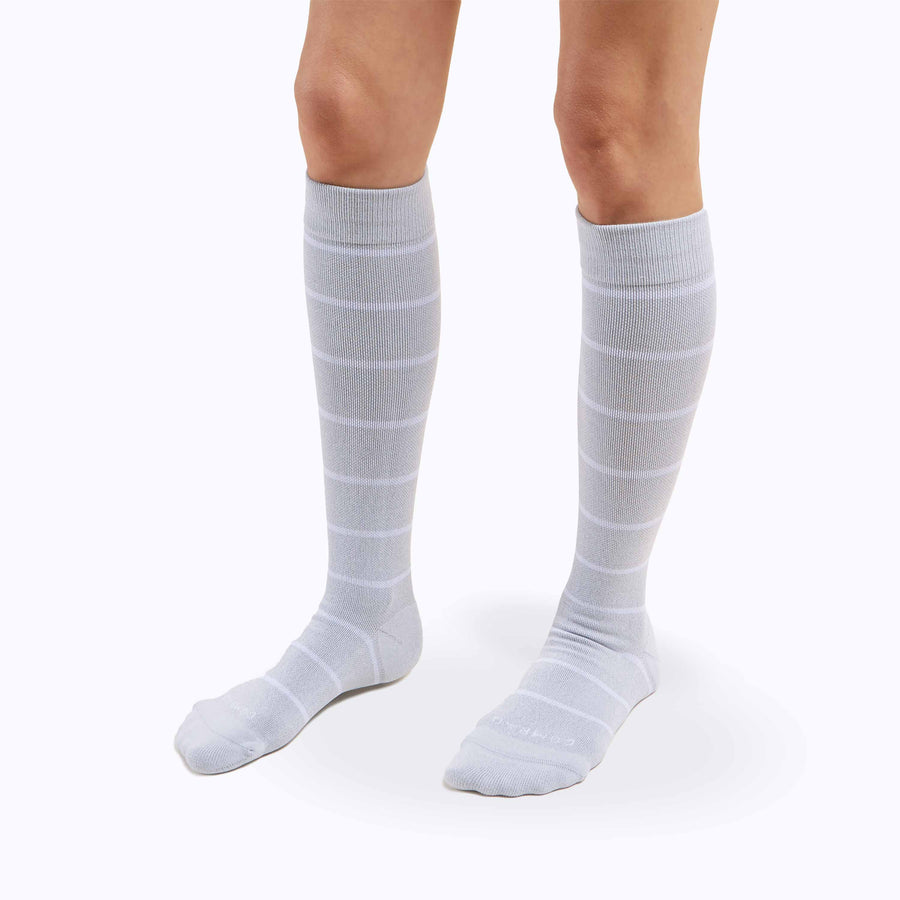 A pair of legs wearing nylon knee high compression socks in heather-white stripes
