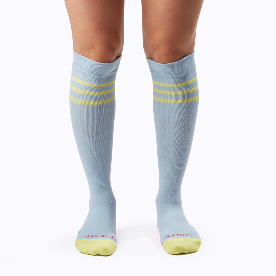 Front view of a pair of legs wearing varstity stripes knee high compression socks in sky blue and pear