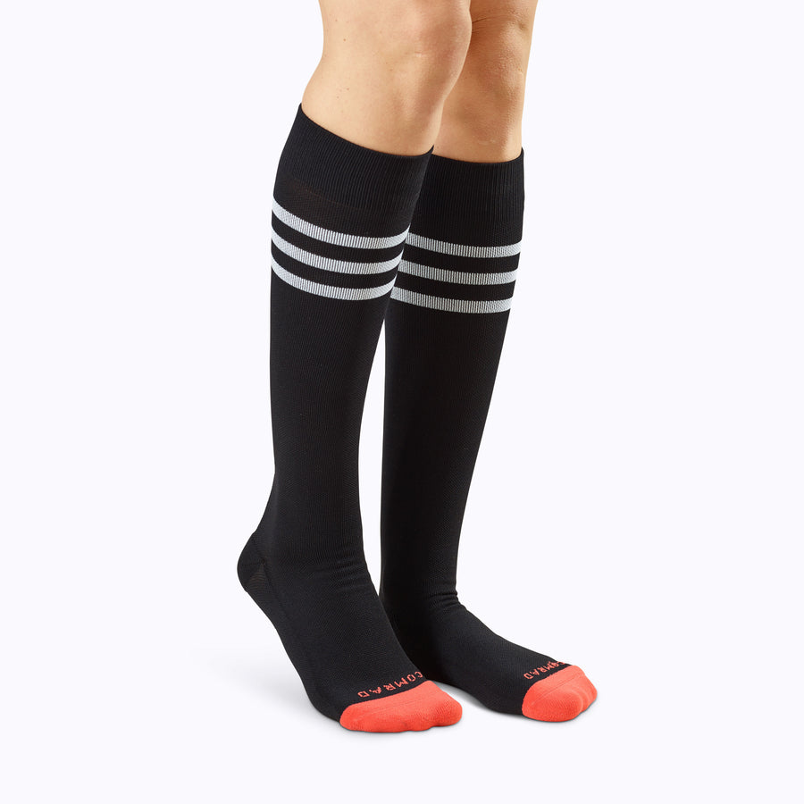 Front view of a pair of legs wearing varstity stripes knee high compression socks in black and white